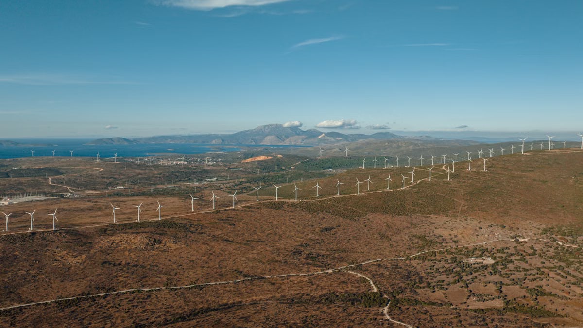 Aerial view of wind turbines on a dry landscape with mountains and sea in Çeşme, İzmir, Turkey.